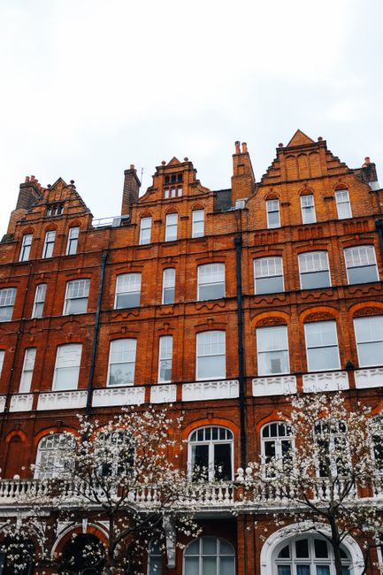 Photograph of the upper floors of a historic, cream-colored Victorian building with multiple rectangular sash windows framed by decorative molding and small balconies with ornate railings. A classic b